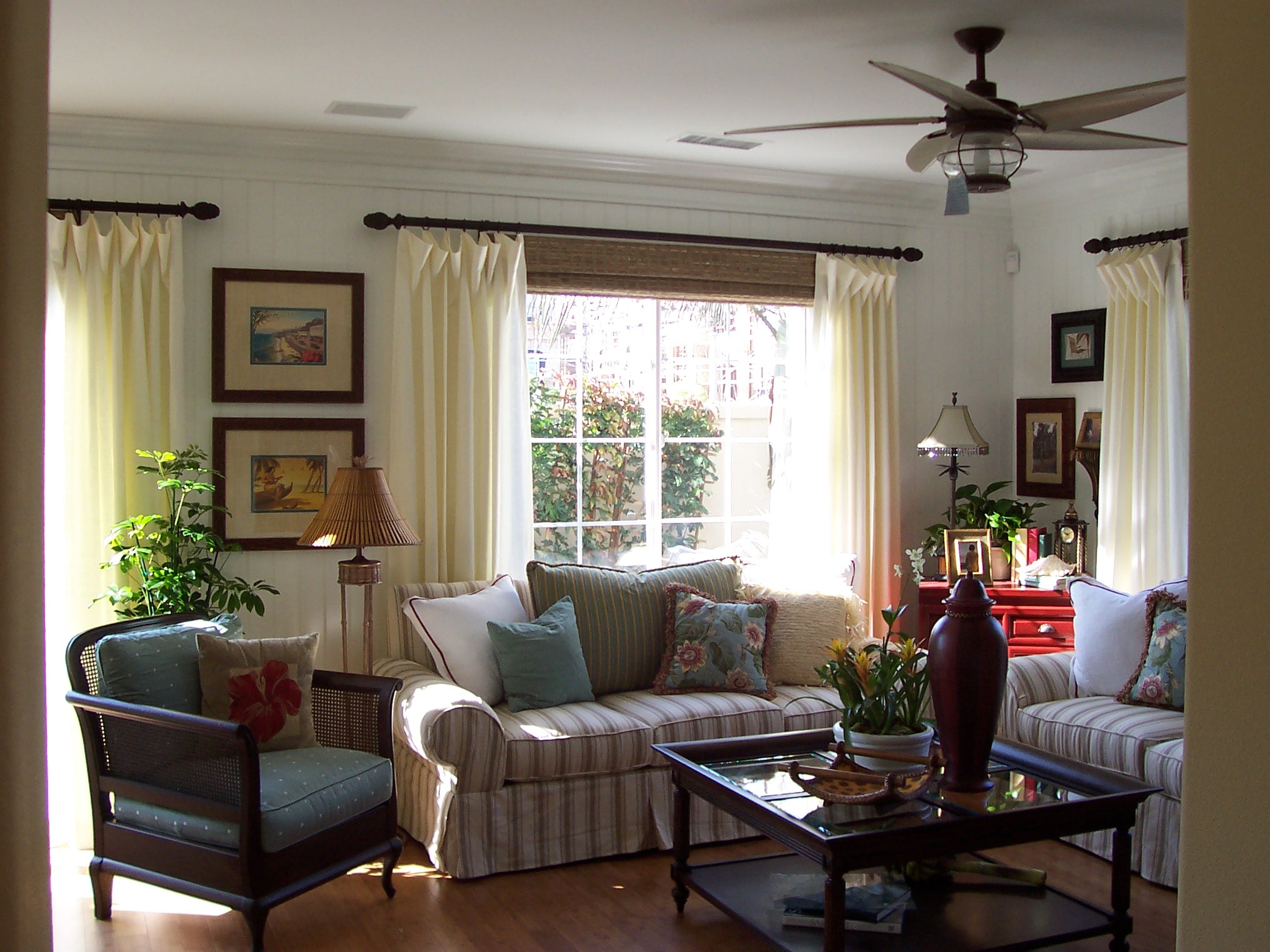Sunlit living room with striped seating, tropical plants, and warm wood furnishings