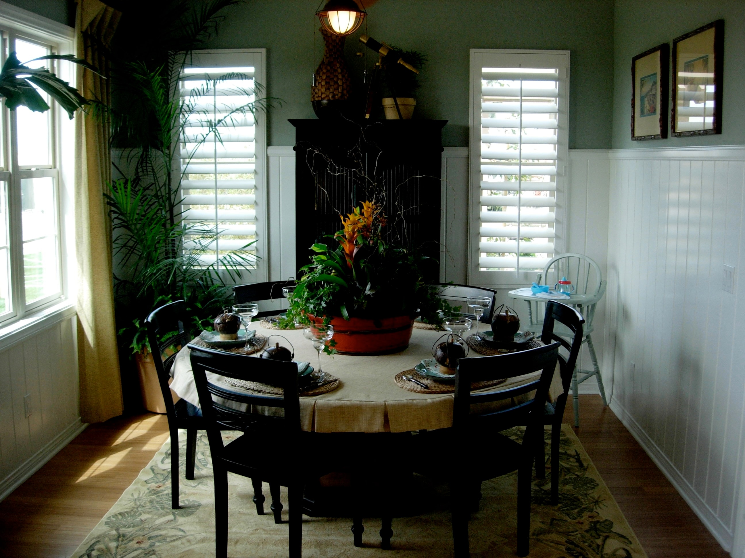 Dining room with a round table, tropical plants, and dark wood furnishings