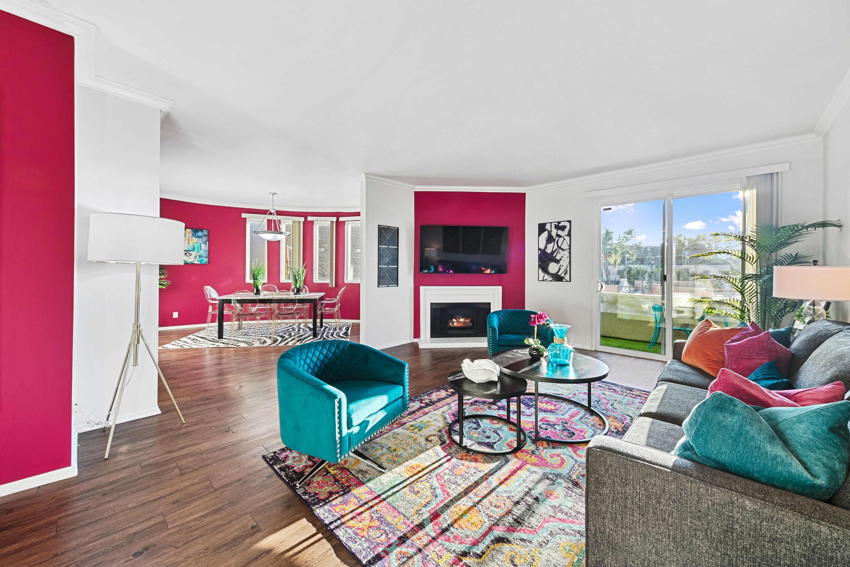 Open-plan living and dining room with teal chairs, fuchsia walls, and patterned rug