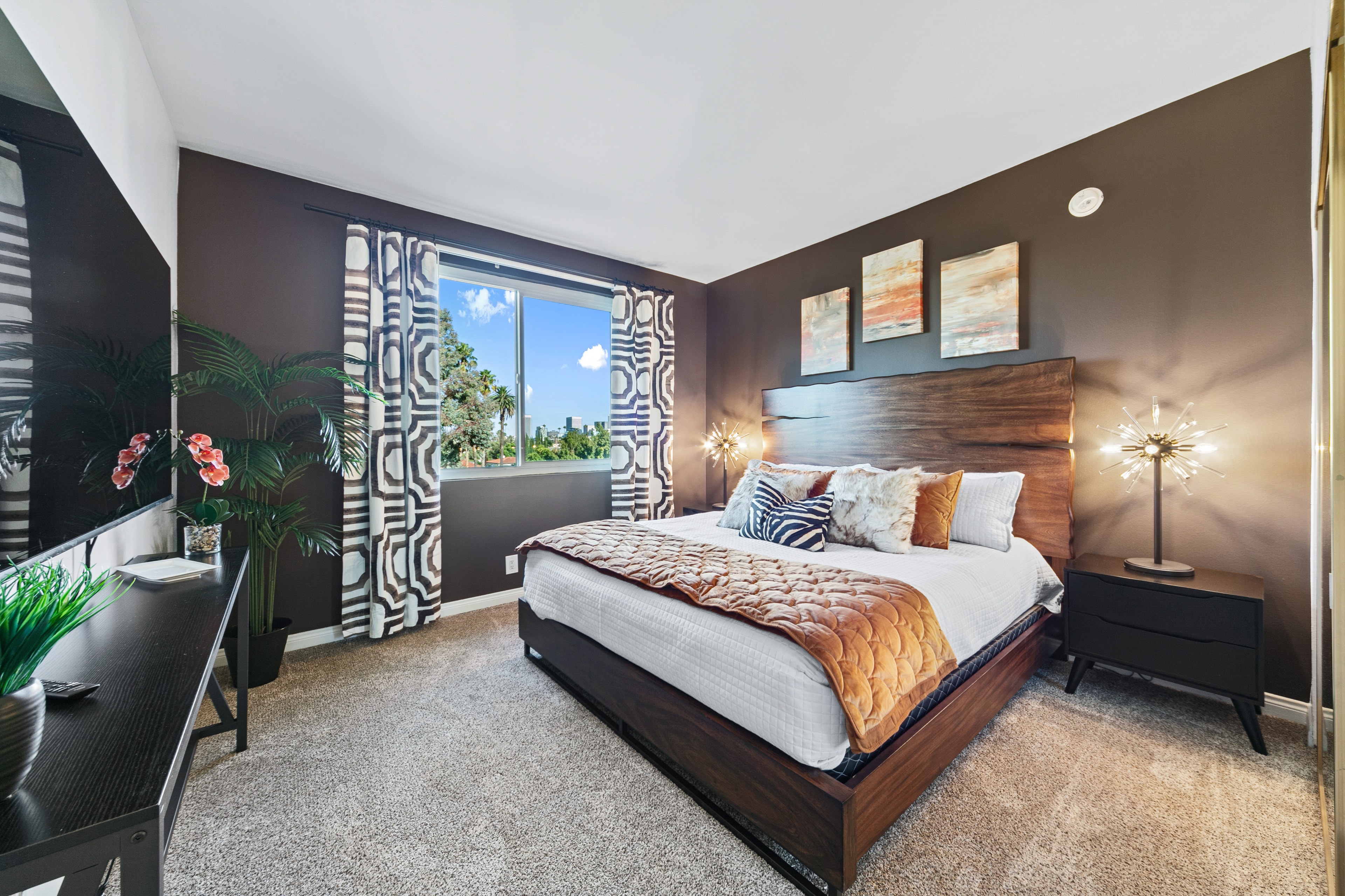 Primary bedroom with dark walls, warm wood headboard, and patterned drapery