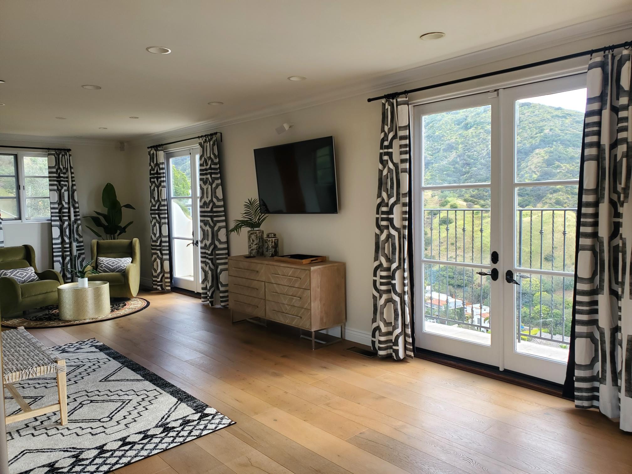 Bedroom sitting area with olive chairs, patterned curtains, and hillside views