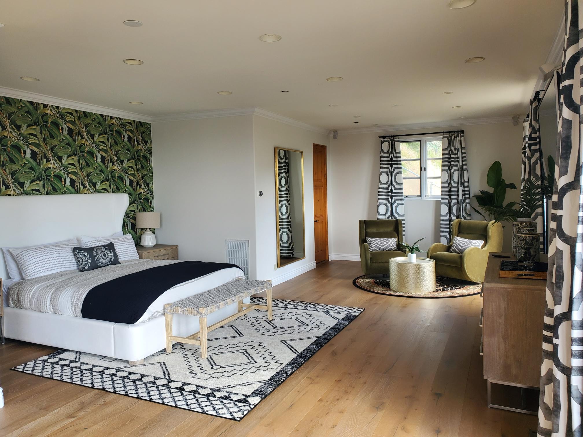 Bedroom with botanical wallpaper, white bed, olive chairs, and patterned curtains
