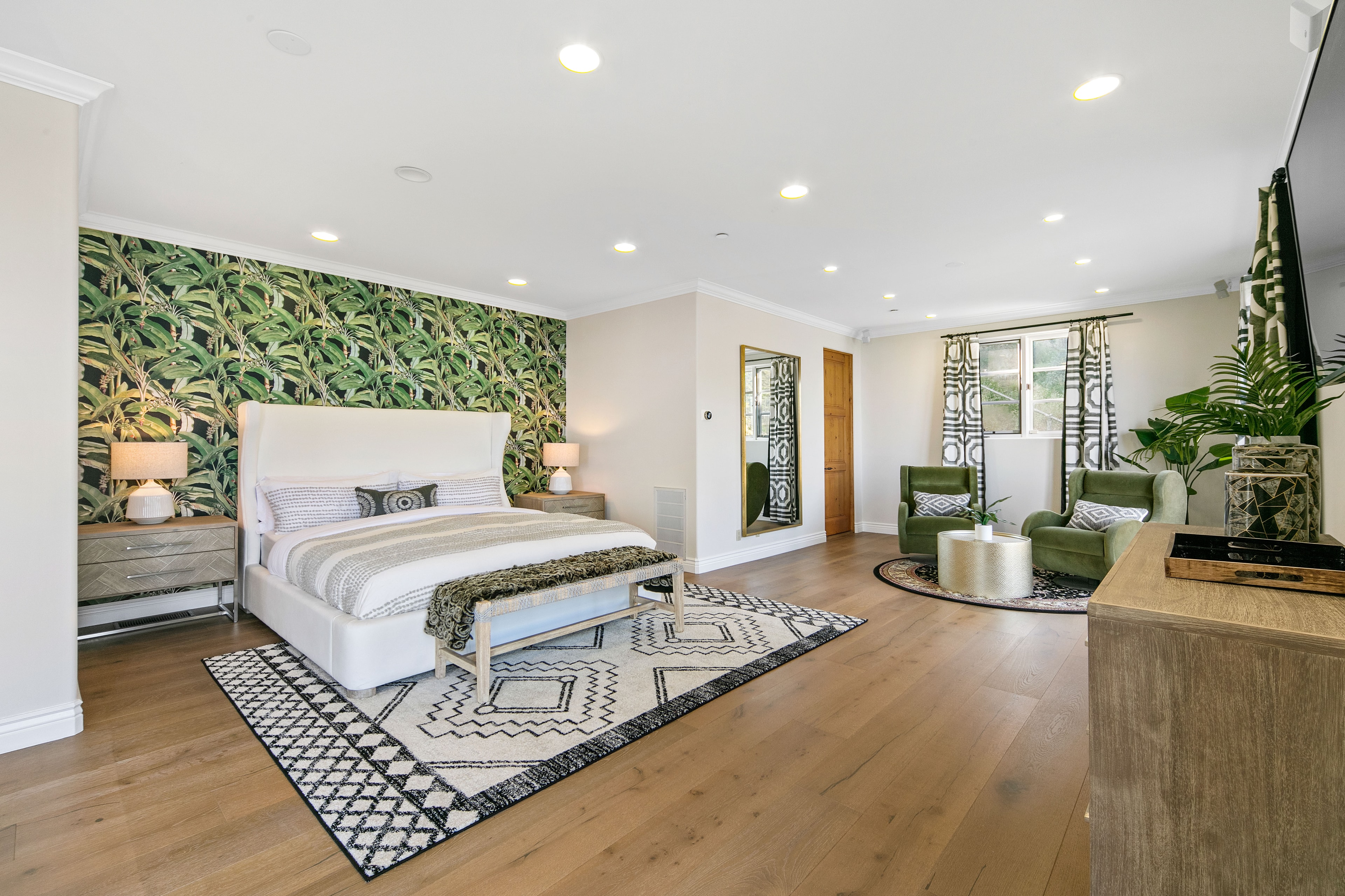 Primary bedroom with botanical wallpaper, white upholstered bed, and green lounge chairs
