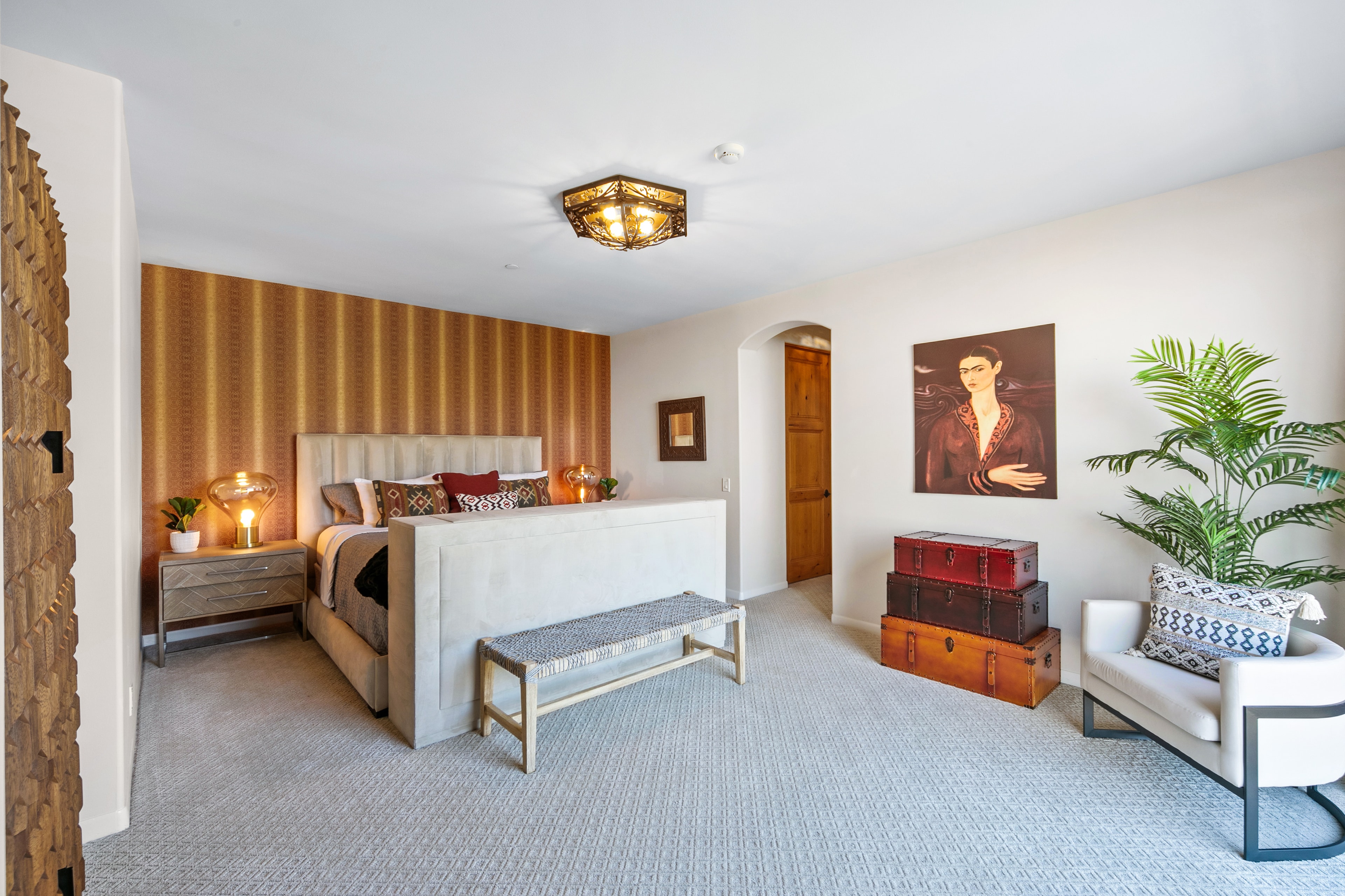 Warm guest bedroom with patterned accent wall, upholstered bed, and vintage trunks