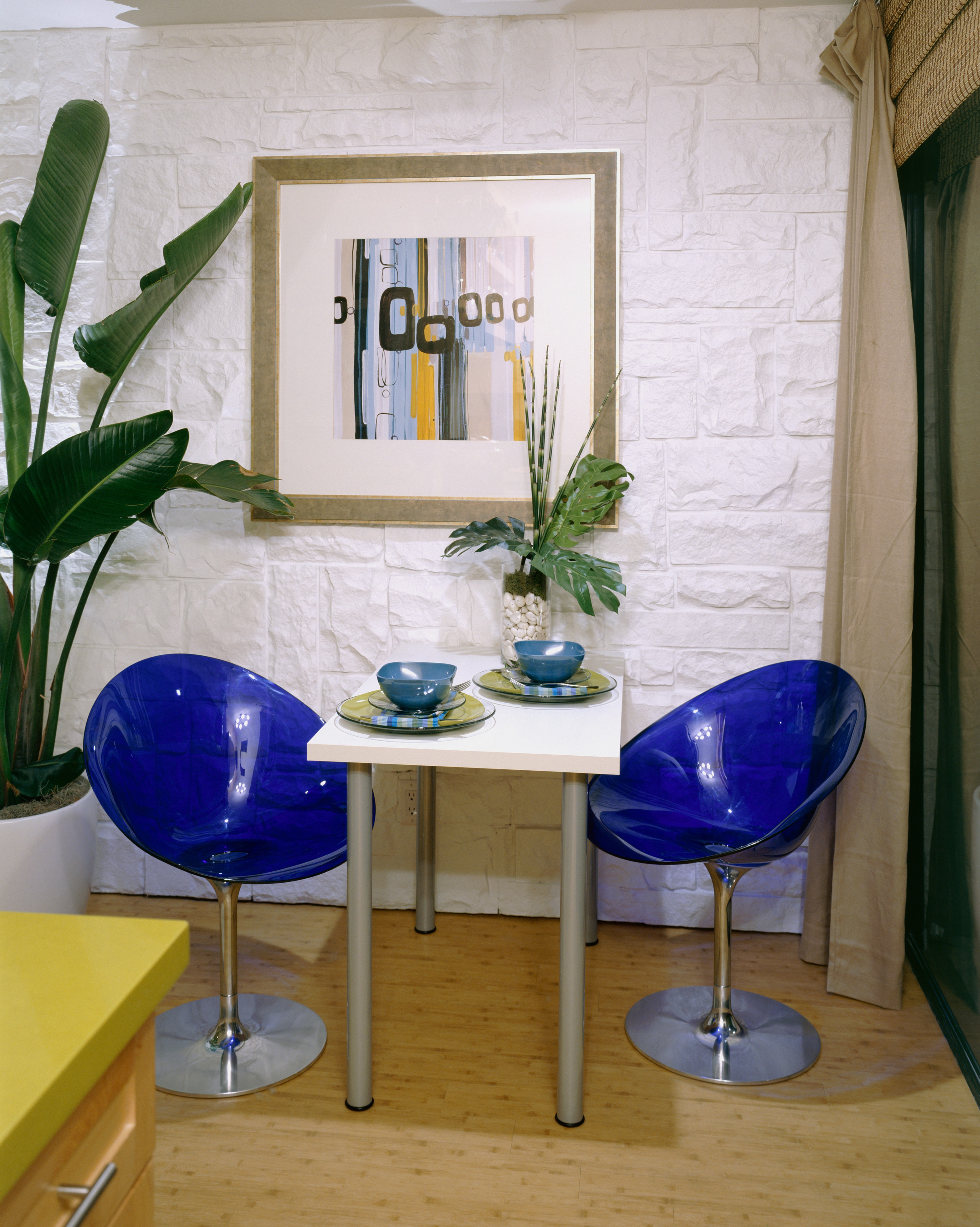 Dining nook with cobalt blue chairs, tropical plants, and a white stone wall