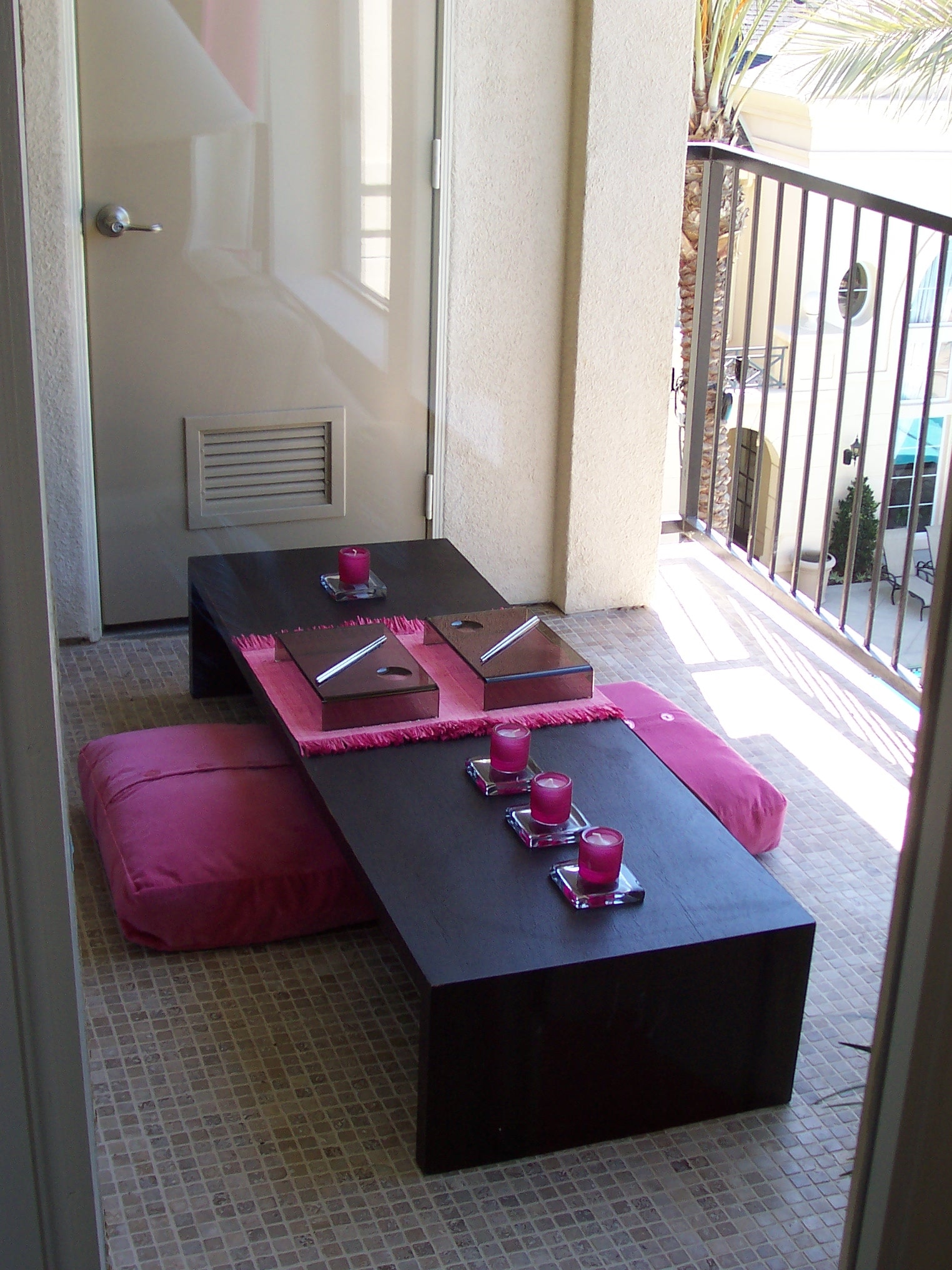 Balcony lounge with low dark wood table, magenta floor cushions, and palm views
