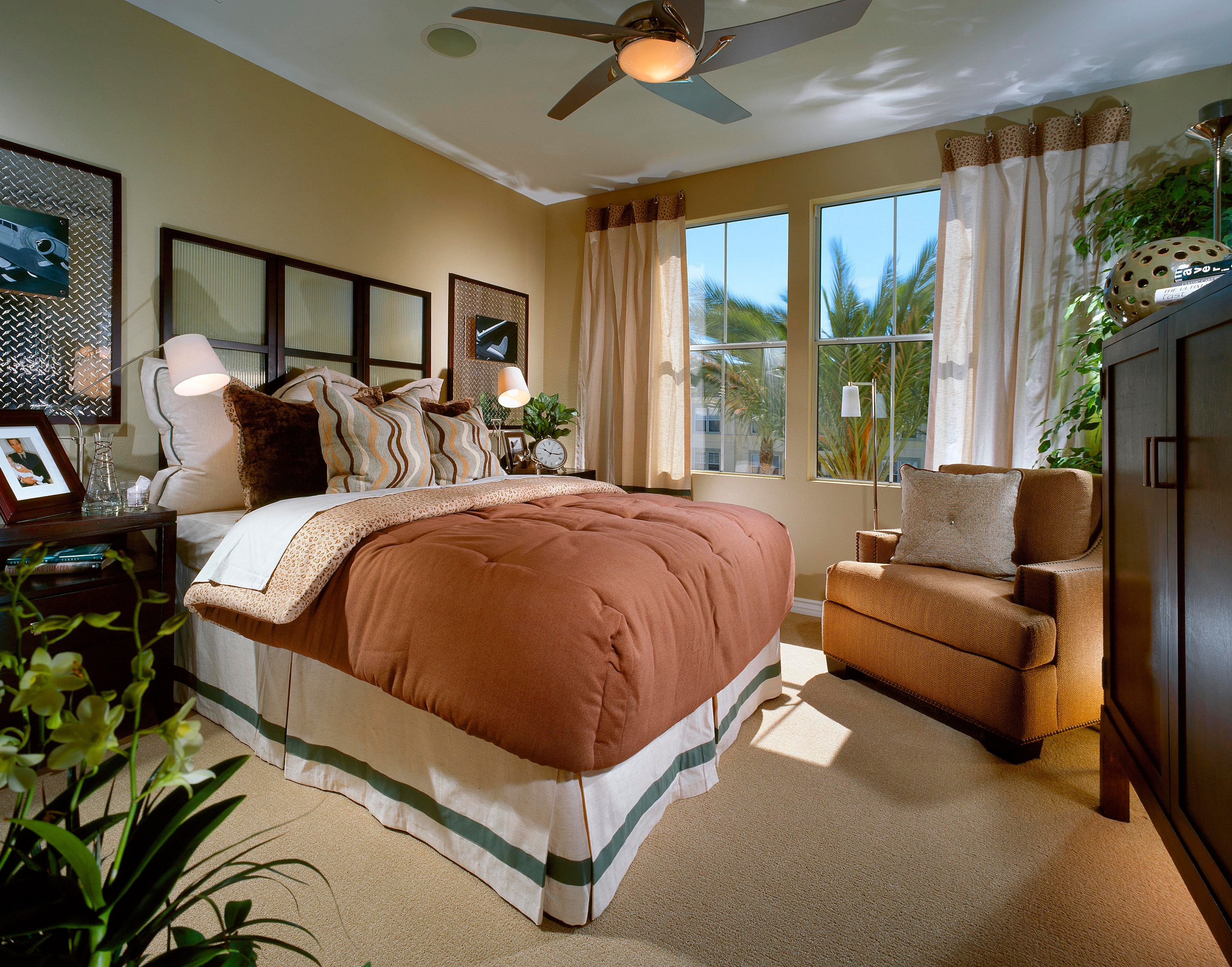Caramel-toned bedroom with layered bedding, dark wood furniture, and palm views