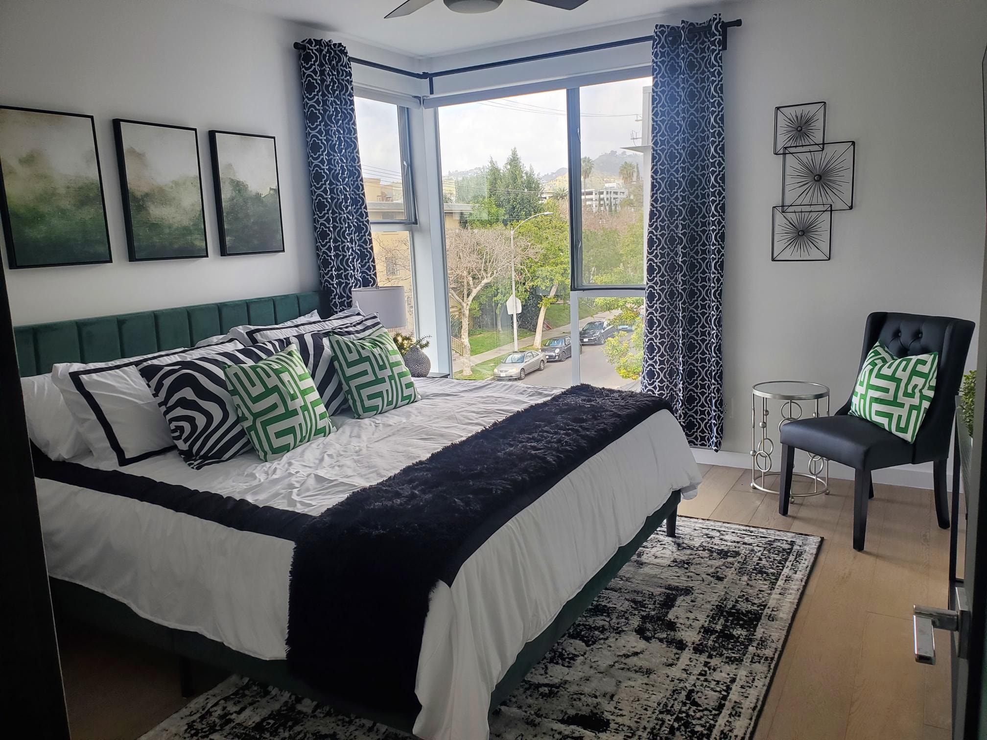 Bedroom with green upholstered bed, black-and-white textiles, and large windows