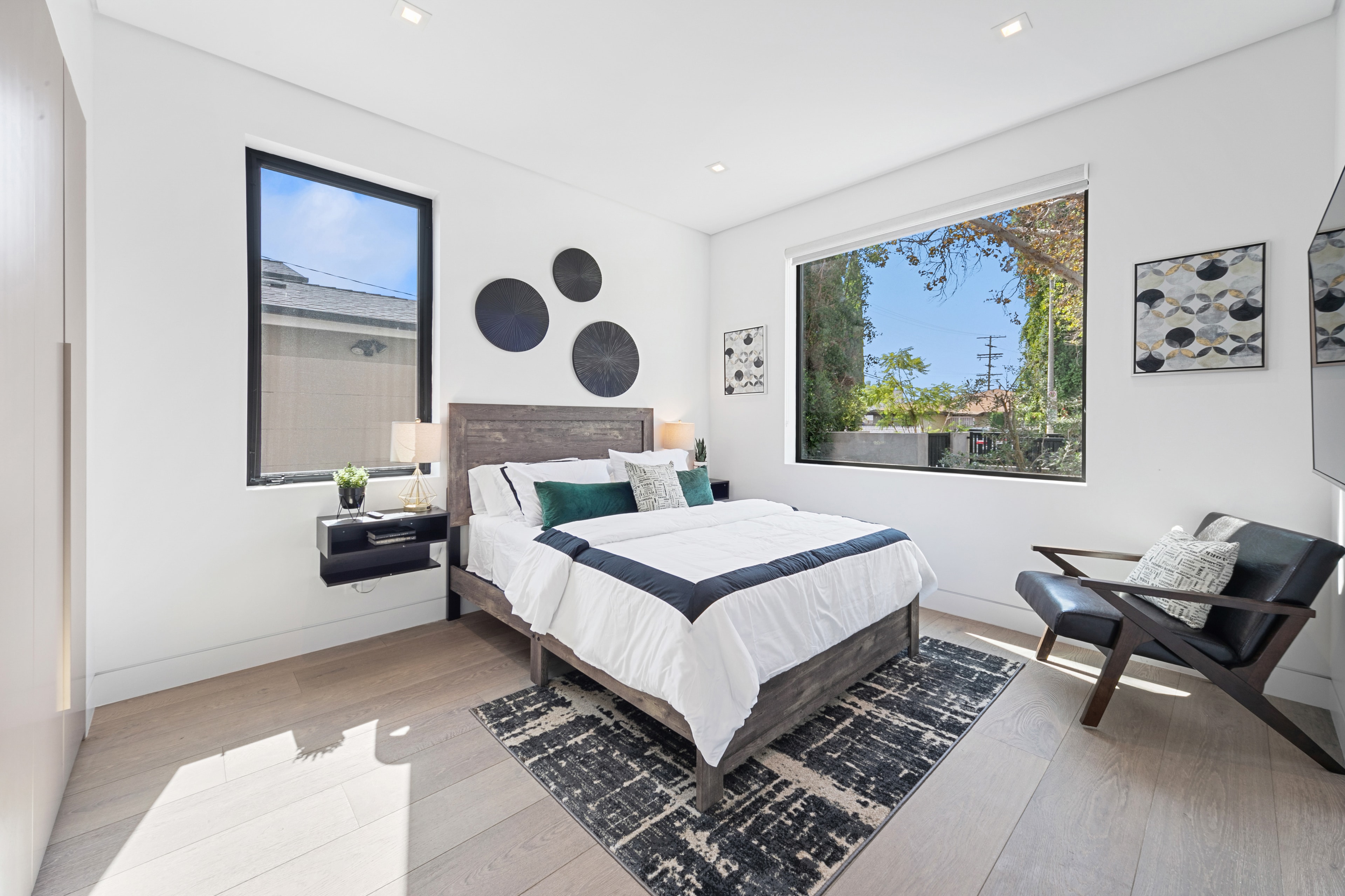 Bright downstairs bedroom with dark wood bed, black accents, and large windows
