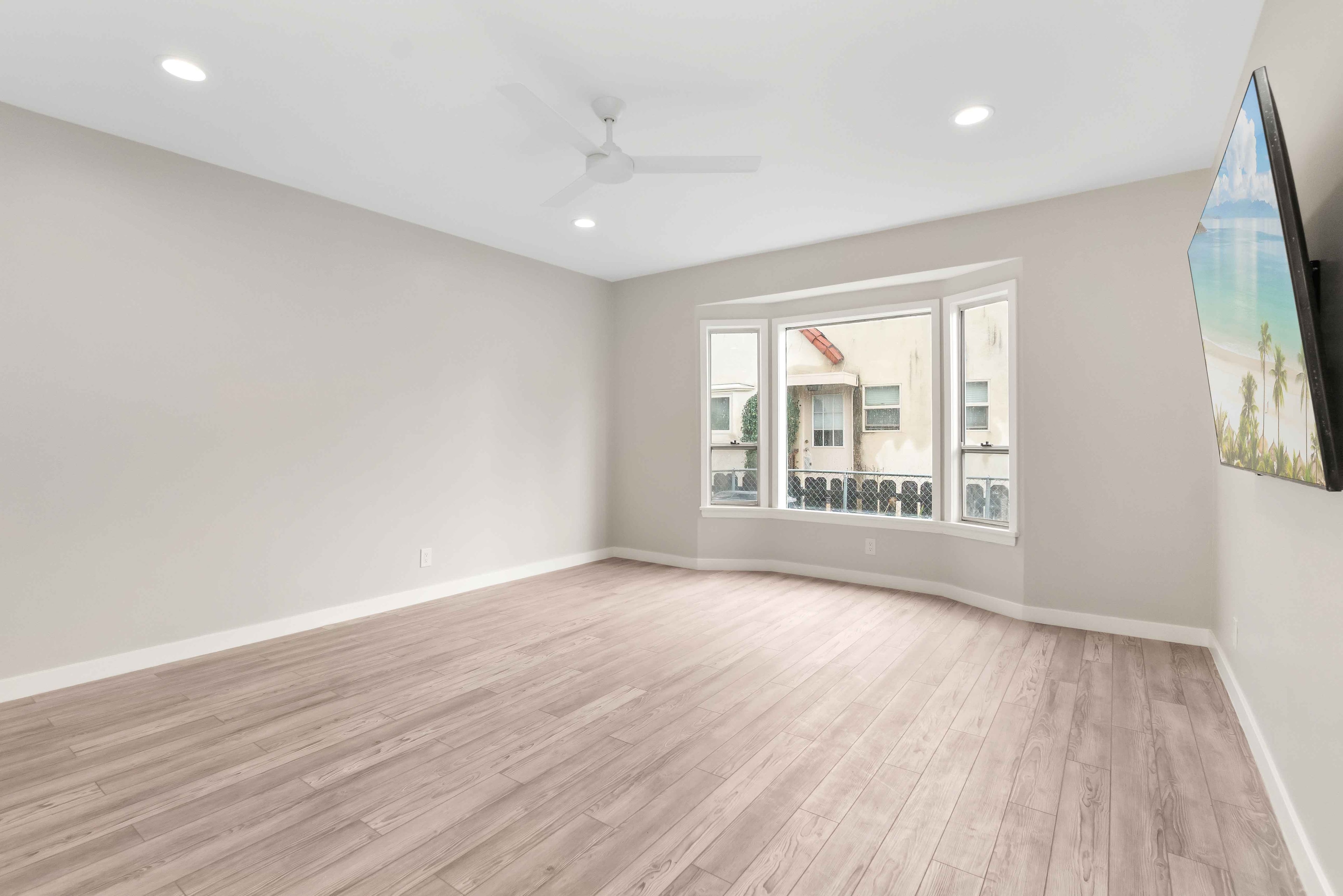 Remodeled living room with bay window, ceiling fan, and wall-mounted television