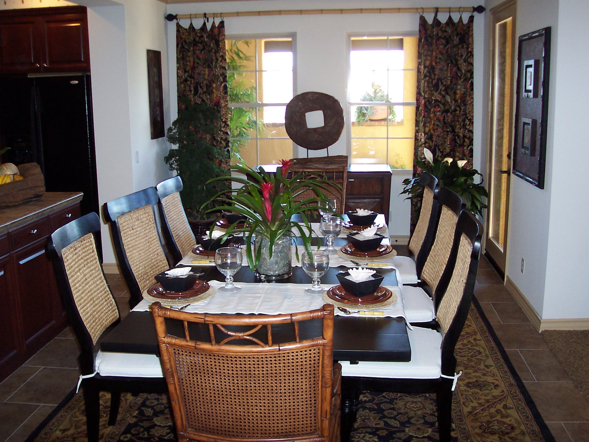Dining table with woven chairs, tropical plants, and dark wood cabinetry
